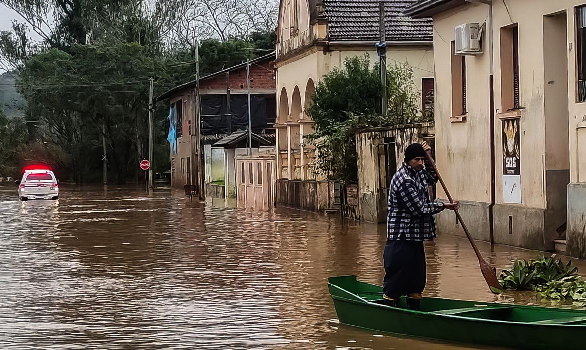 Homem andando de canoa em uma rua completamente alagada 